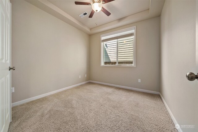 empty room featuring light carpet, a raised ceiling, and ceiling fan