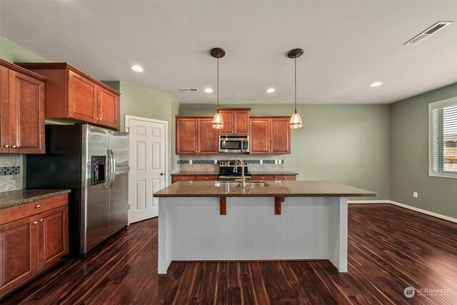 kitchen with appliances with stainless steel finishes, a center island with sink, and dark wood-type flooring