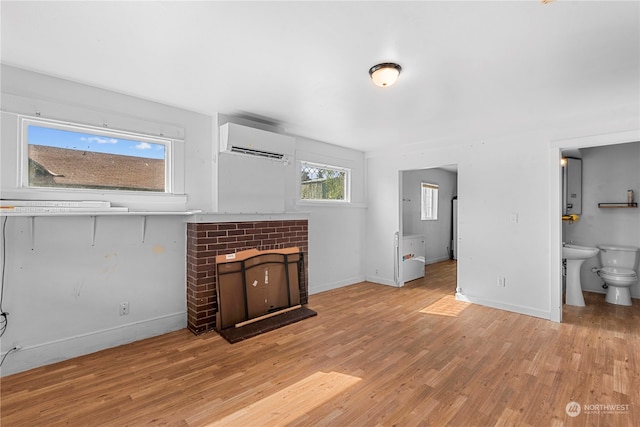 living room featuring a wall mounted AC, a brick fireplace, sink, and light hardwood / wood-style floors