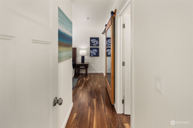 corridor with a barn door, baseboards, and dark wood-type flooring