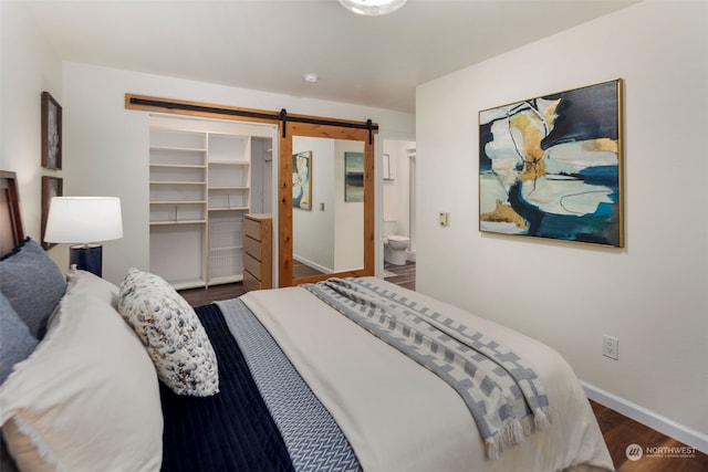 bedroom featuring ensuite bath, wood finished floors, a barn door, a closet, and baseboards