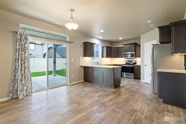 kitchen with dark brown cabinetry, hanging light fixtures, kitchen peninsula, hardwood / wood-style flooring, and appliances with stainless steel finishes