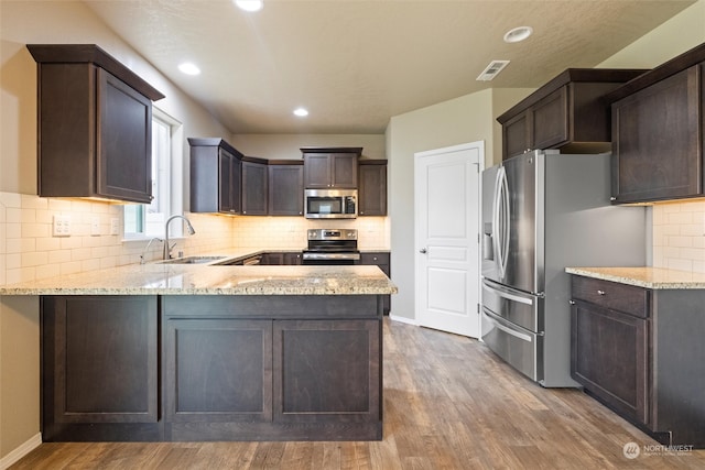 kitchen with hardwood / wood-style flooring, sink, kitchen peninsula, appliances with stainless steel finishes, and light stone countertops