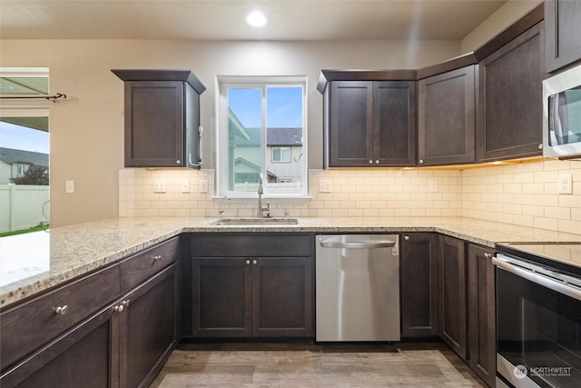 kitchen with sink, backsplash, appliances with stainless steel finishes, hardwood / wood-style floors, and light stone countertops