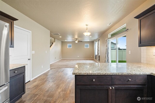 kitchen with dark brown cabinets, light wood-type flooring, light stone counters, a textured ceiling, and ceiling fan