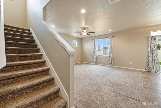 stairway with ceiling fan, hardwood / wood-style floors, and a textured ceiling