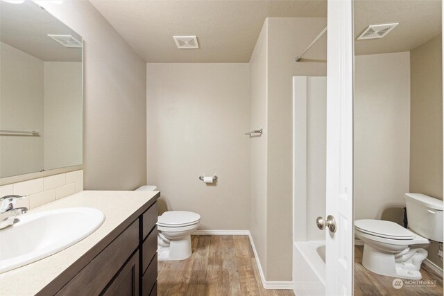 full bathroom with a textured ceiling, hardwood / wood-style flooring, shower / tub combination, vanity, and toilet