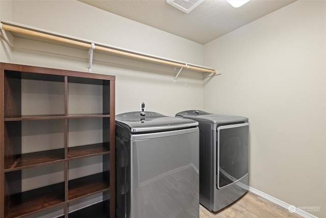 clothes washing area featuring light wood-type flooring, a textured ceiling, and washing machine and clothes dryer