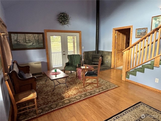 living area with a wood stove, hardwood / wood-style floors, a high ceiling, and french doors