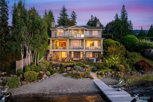 back of house with stone siding, stairway, a balcony, a chimney, and a patio area