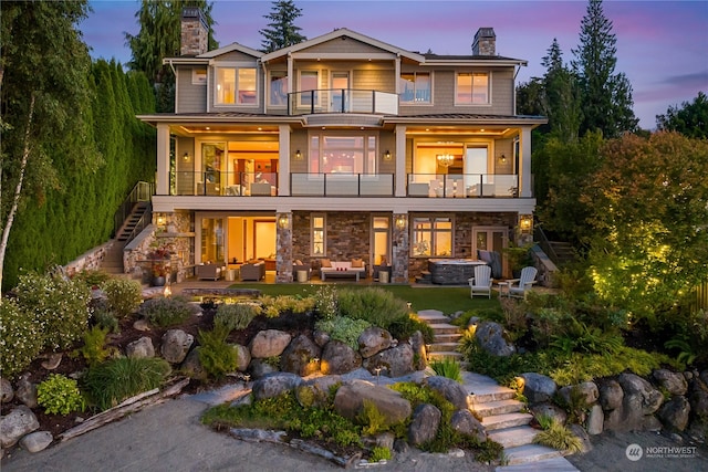 back house at dusk with a balcony, a patio, and outdoor lounge area