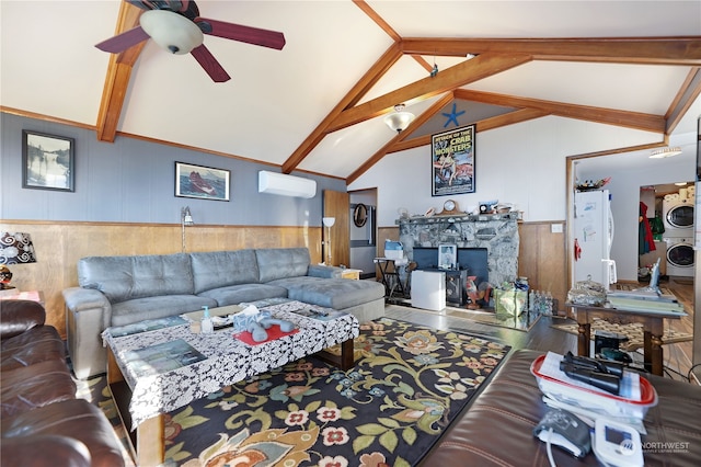 living room with stacked washing maching and dryer, ceiling fan, a stone fireplace, and vaulted ceiling with beams