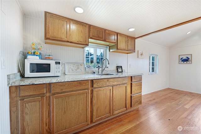 kitchen featuring ornamental molding, light hardwood / wood-style flooring, light stone counters, sink, and vaulted ceiling