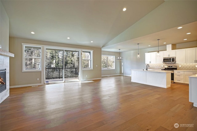 unfurnished living room featuring high vaulted ceiling, a fireplace, light hardwood / wood-style floors, and sink