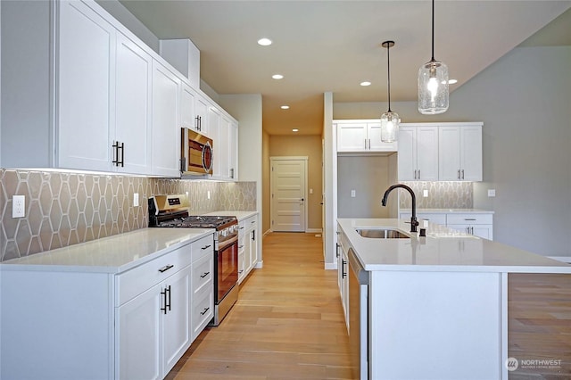 kitchen featuring sink, hanging light fixtures, an island with sink, stainless steel appliances, and white cabinets