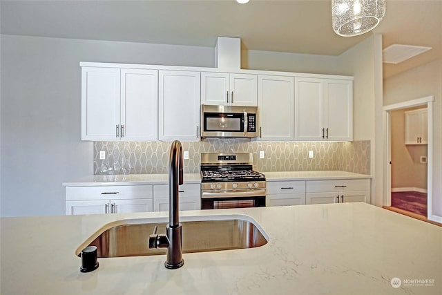 kitchen featuring sink, white cabinetry, hanging light fixtures, appliances with stainless steel finishes, and backsplash