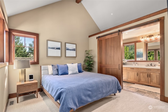 bedroom featuring light carpet, high vaulted ceiling, ensuite bathroom, and a barn door