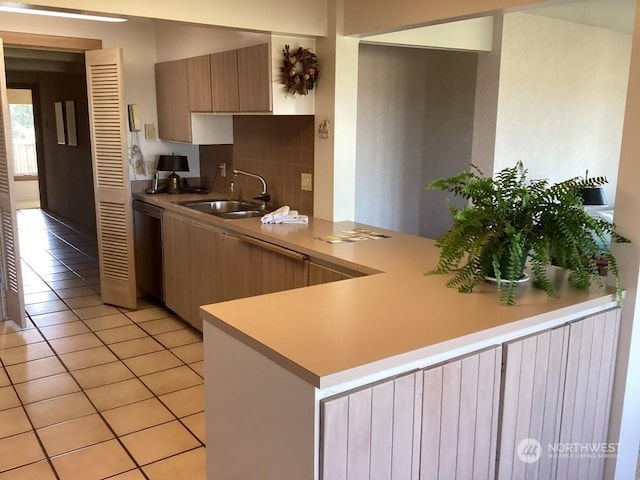 kitchen featuring sink, stainless steel dishwasher, kitchen peninsula, decorative backsplash, and light tile patterned floors