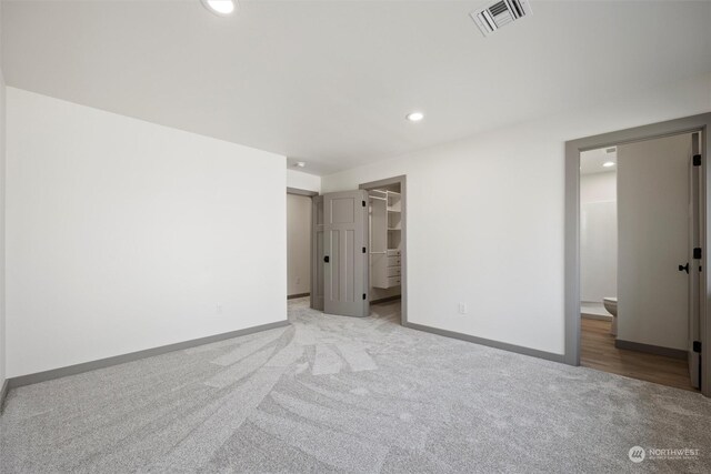 unfurnished bedroom featuring a closet, a spacious closet, ensuite bathroom, and light colored carpet