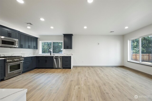 kitchen with light stone countertops, stainless steel appliances, light hardwood / wood-style floors, and sink