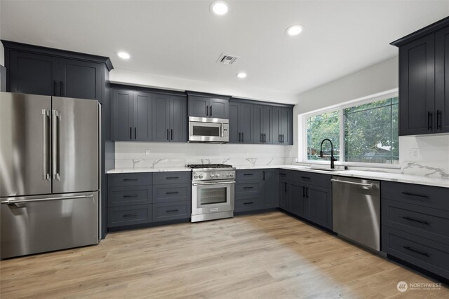 kitchen with sink, light stone countertops, appliances with stainless steel finishes, and light hardwood / wood-style floors