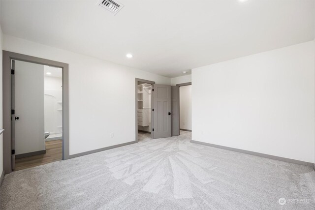 unfurnished bedroom with a walk in closet, light colored carpet, a closet, and ensuite bath