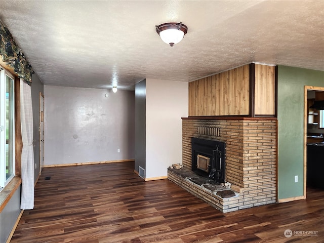 unfurnished living room with dark wood-type flooring, a textured ceiling, and a brick fireplace