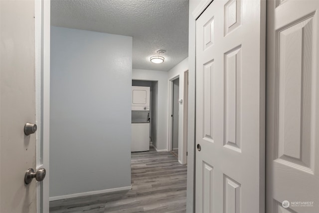 hall featuring wood-type flooring, a textured ceiling, and stacked washer / drying machine