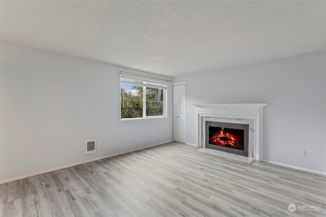 unfurnished living room with light hardwood / wood-style floors, a premium fireplace, and a textured ceiling