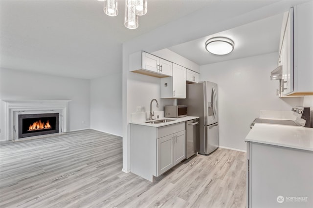 kitchen featuring white cabinetry, sink, stainless steel appliances, a fireplace, and exhaust hood