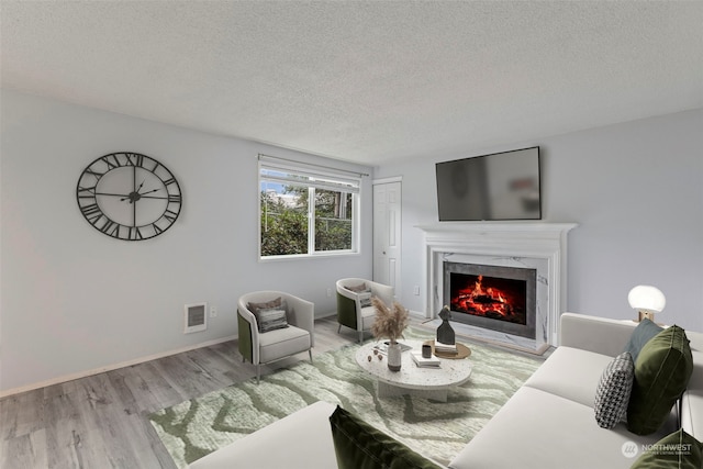 living room featuring a high end fireplace, light hardwood / wood-style floors, and a textured ceiling