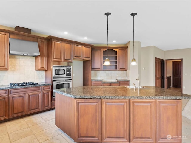 kitchen featuring an island with sink, stainless steel appliances, sink, and wall chimney exhaust hood