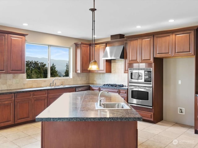 kitchen with stainless steel appliances, sink, wall chimney range hood, and a kitchen island with sink