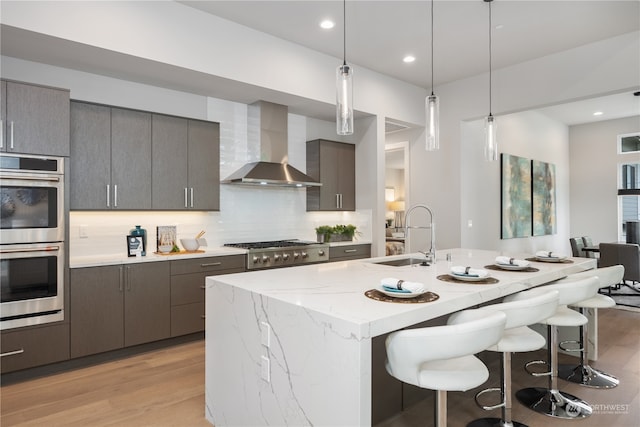 kitchen with light hardwood / wood-style flooring, appliances with stainless steel finishes, wall chimney range hood, and decorative light fixtures