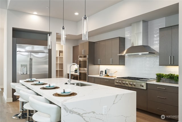 kitchen with a kitchen island with sink, stainless steel appliances, wall chimney range hood, and light hardwood / wood-style floors