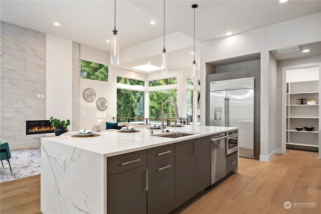 kitchen with a kitchen island with sink, light hardwood / wood-style flooring, stainless steel appliances, a tile fireplace, and sink