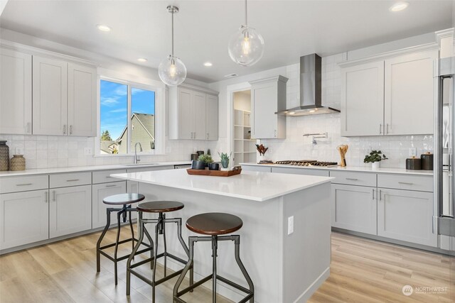 kitchen with stainless steel gas cooktop, wall chimney range hood, a kitchen island, hanging light fixtures, and light hardwood / wood-style floors