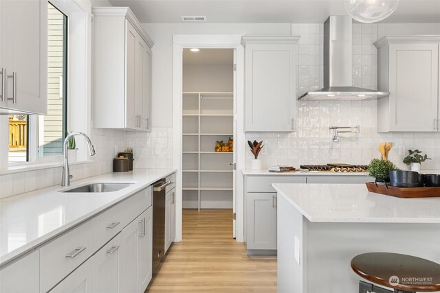 kitchen with wall chimney exhaust hood, light hardwood / wood-style flooring, sink, and decorative backsplash