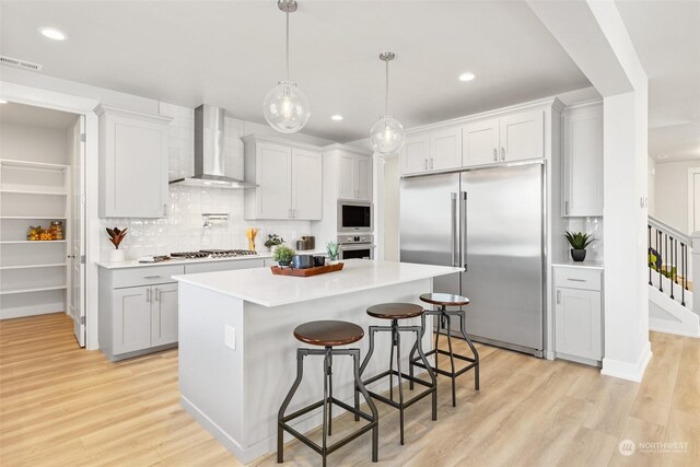 kitchen featuring a center island, light hardwood / wood-style flooring, wall chimney range hood, built in appliances, and a kitchen bar