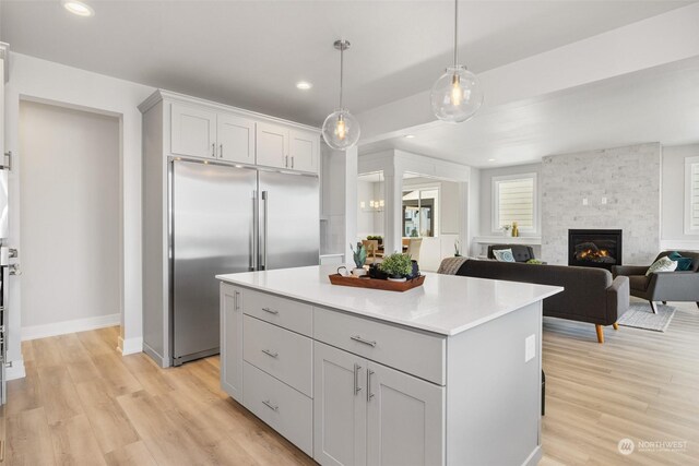 kitchen with a kitchen island, built in fridge, pendant lighting, a stone fireplace, and light hardwood / wood-style floors