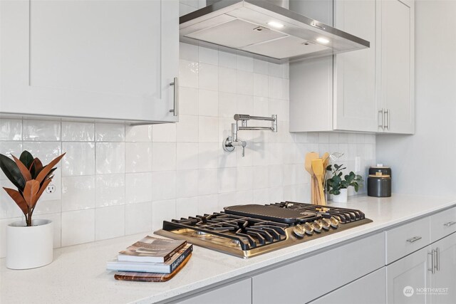 kitchen featuring stainless steel gas cooktop, decorative backsplash, wall chimney exhaust hood, and white cabinetry