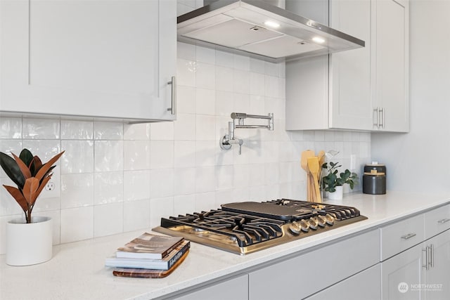 kitchen with light stone countertops, stainless steel gas cooktop, white cabinets, wall chimney exhaust hood, and tasteful backsplash