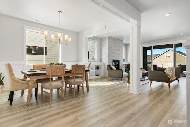 dining area featuring a wainscoted wall, visible vents, a stone fireplace, light wood-style floors, and a notable chandelier