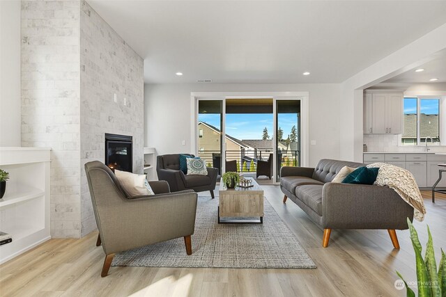 living room featuring sink, a stone fireplace, and light wood-type flooring