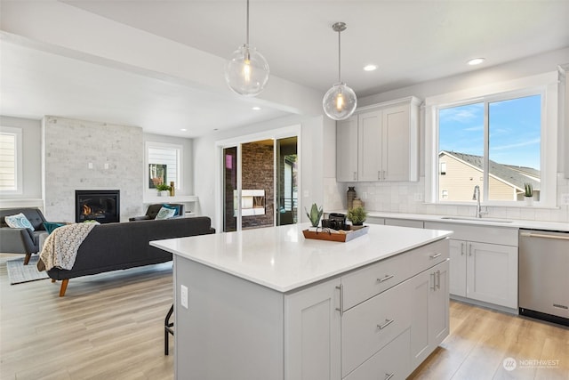 kitchen featuring light wood finished floors, backsplash, a large fireplace, dishwasher, and a sink