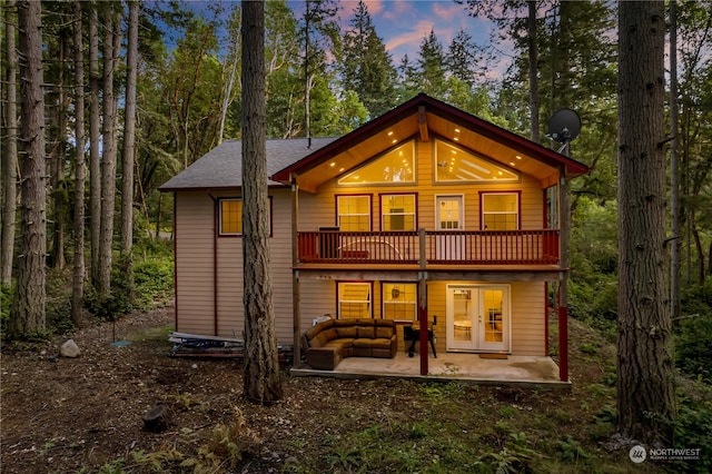 back house at dusk featuring a balcony, an outdoor living space, and a patio area