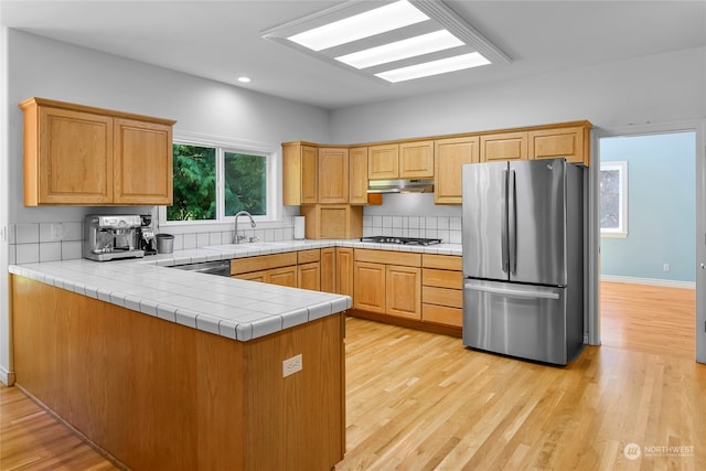 kitchen with sink, kitchen peninsula, light hardwood / wood-style flooring, appliances with stainless steel finishes, and tile countertops