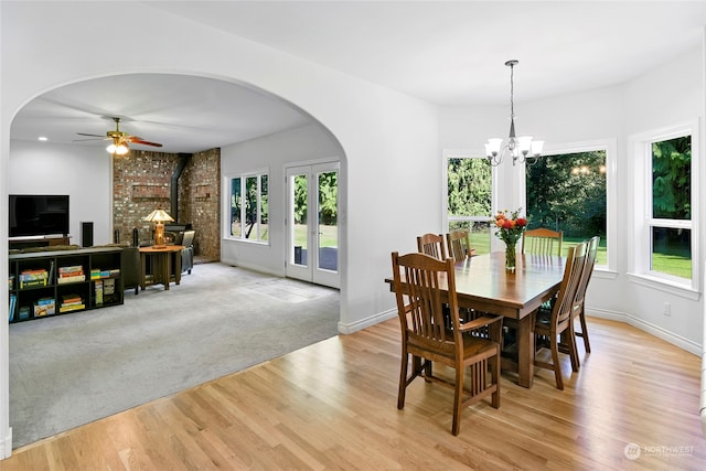 dining area with ceiling fan with notable chandelier, a wealth of natural light, a wood stove, and light hardwood / wood-style floors