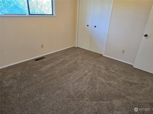 unfurnished bedroom with dark colored carpet and a closet