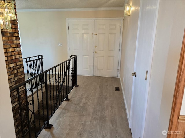 hallway featuring wood finished floors, an upstairs landing, visible vents, and ornamental molding